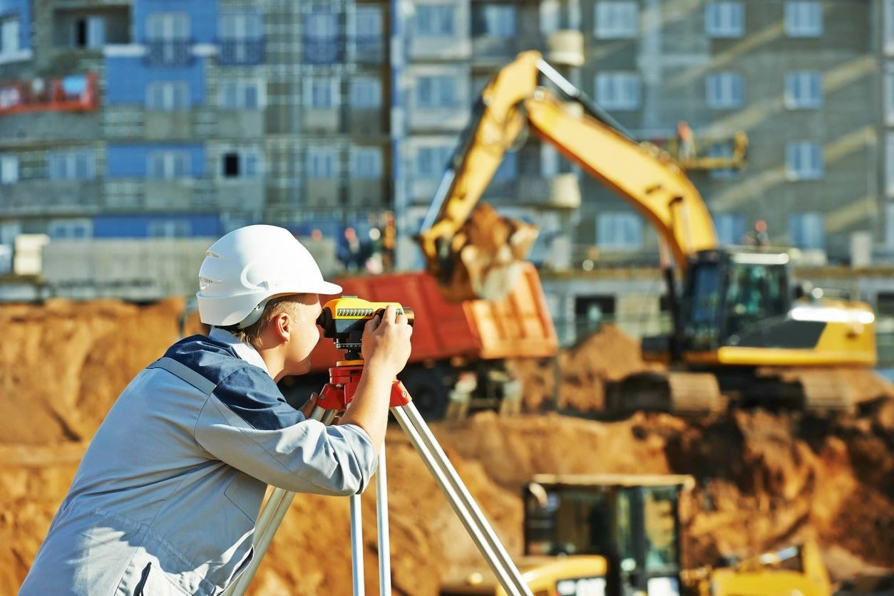 A man in white hard hat using a surveying tool.