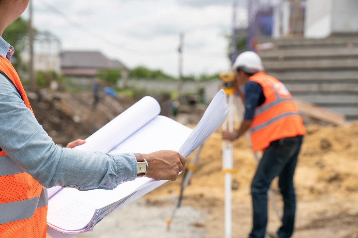 A man holding construction plans while another man is working on something.