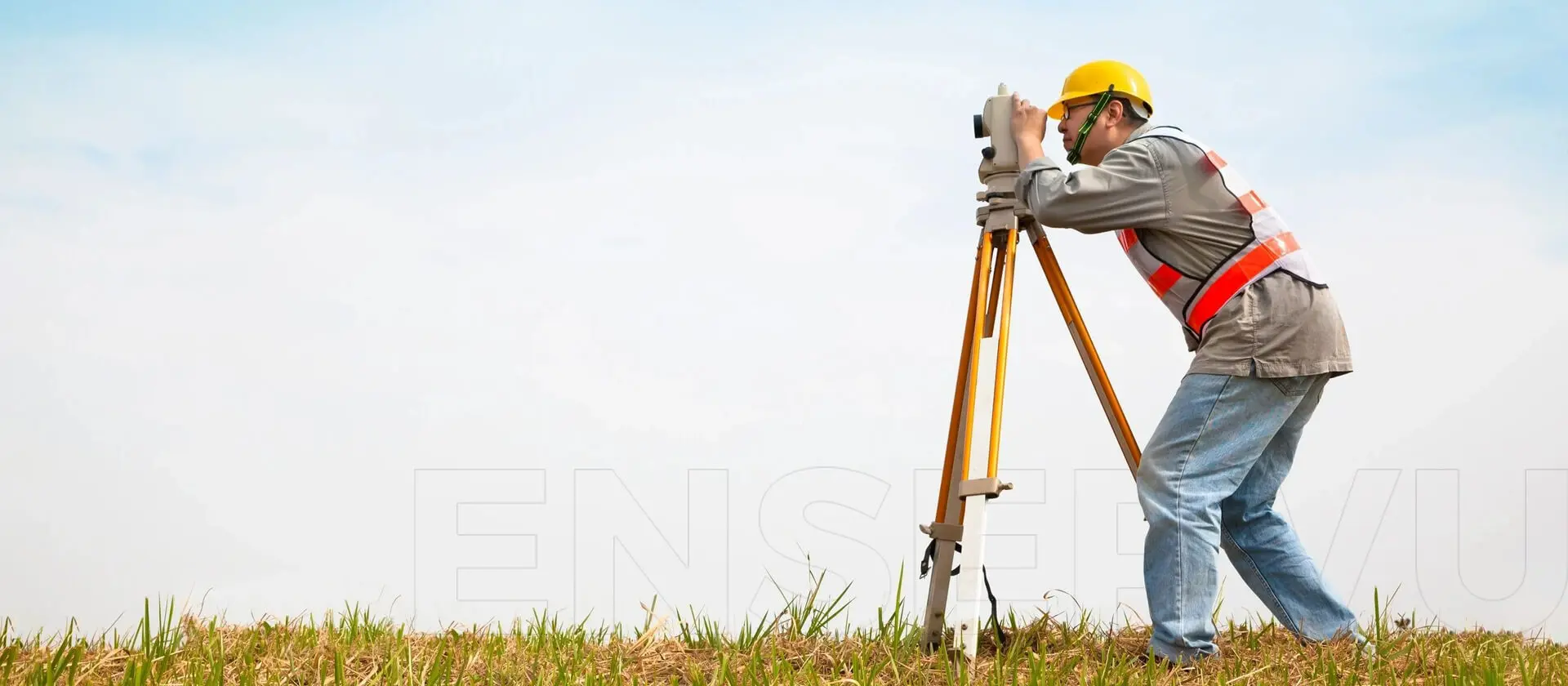 A man in yellow hard hat using a surveying equipment.